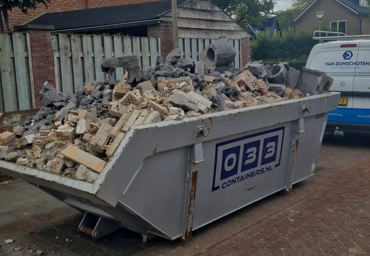 Bouwcontainer van 033 Containers volgeladen met puin en sloopafval op de oprit bij een woning