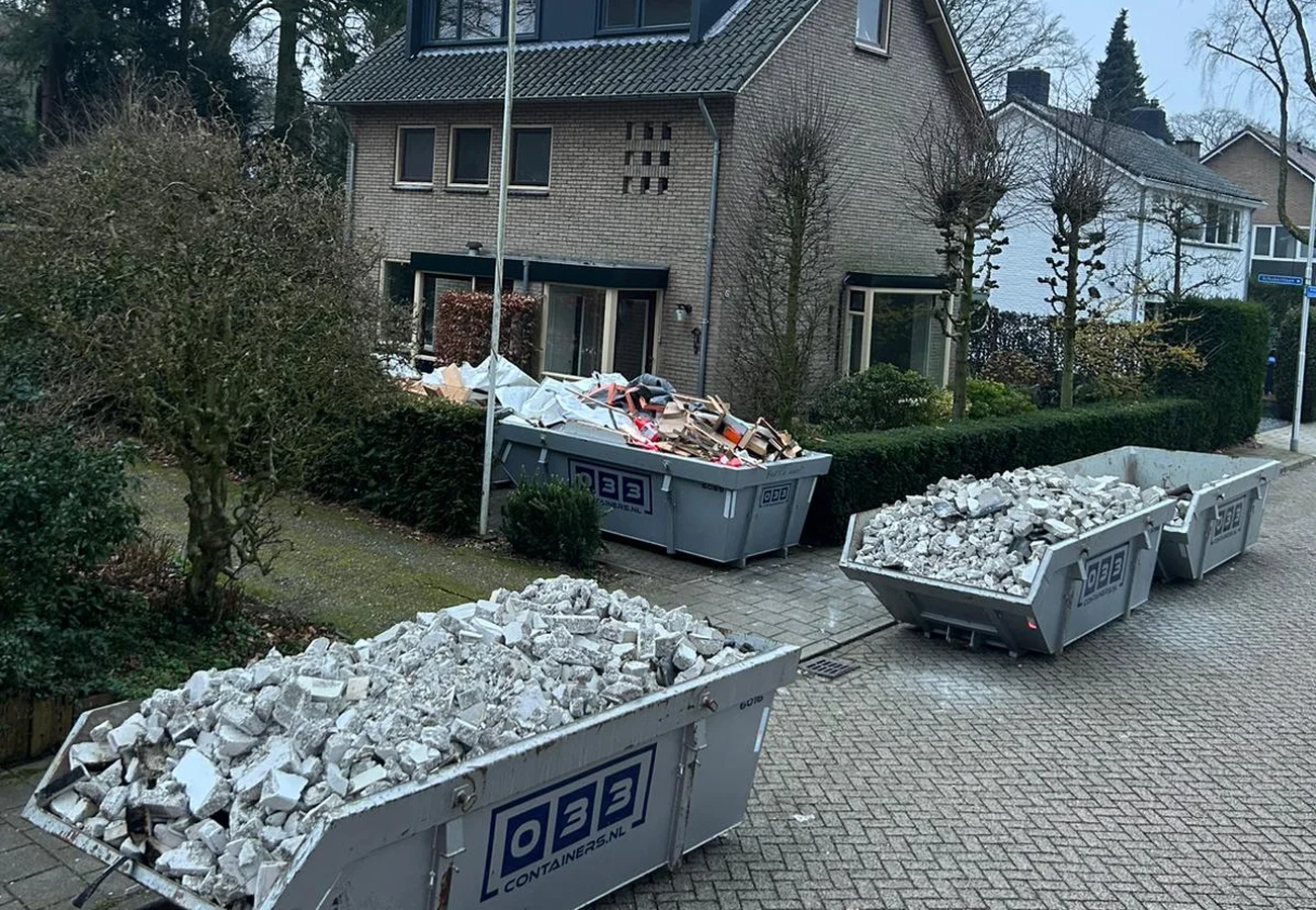 Drie puinafvalcontainers van 033 Containers gevuld met sloopafval, geplaatst op straat voor een woonhuis
